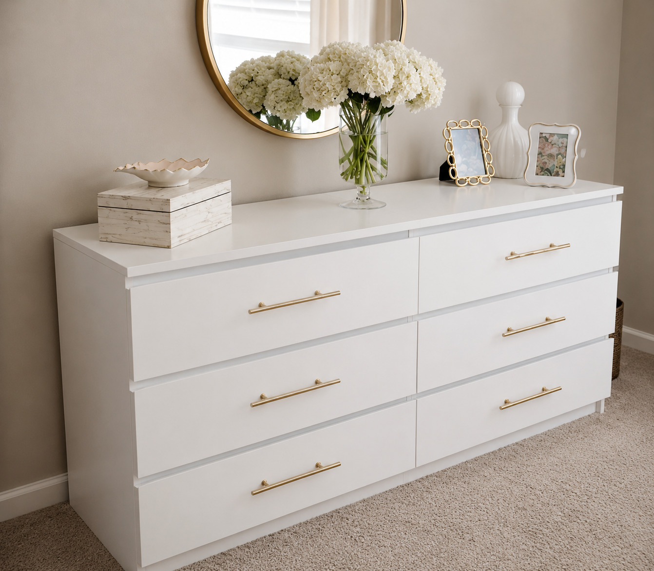 Bloom white 6-drawer chest of drawers with brass bar handles, styled beneath a round mirror with hydrangeas and photo frames