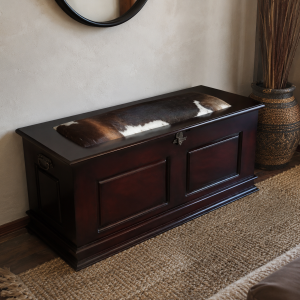 Isiko Kist, a dark solid wood lobola kist with a cowhide-cushioned lid and brass lock, styled in a living room